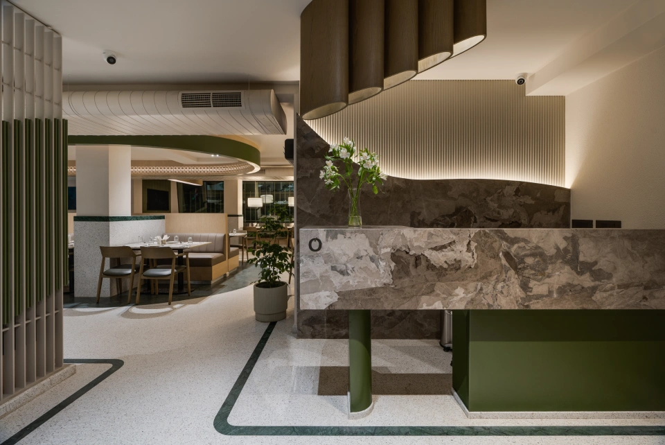 Reception counter finished in dark marble and green millwork beneath a sculptural pendant light