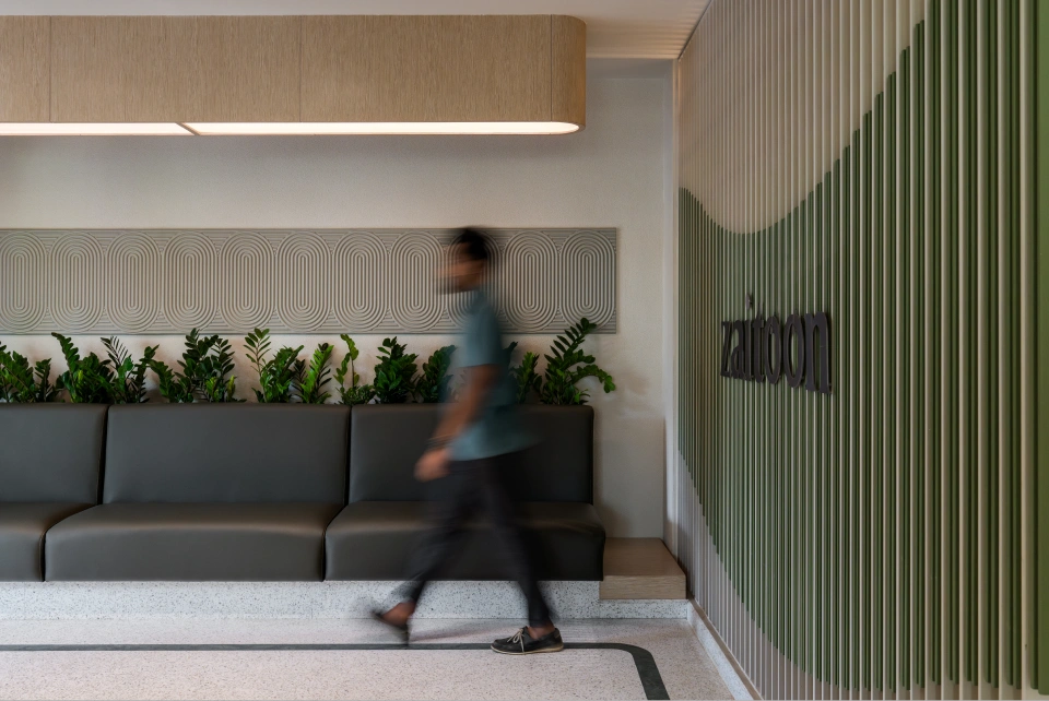 A guest walking past the lounge seating and patterned wall panel beside the Zaitoon signage