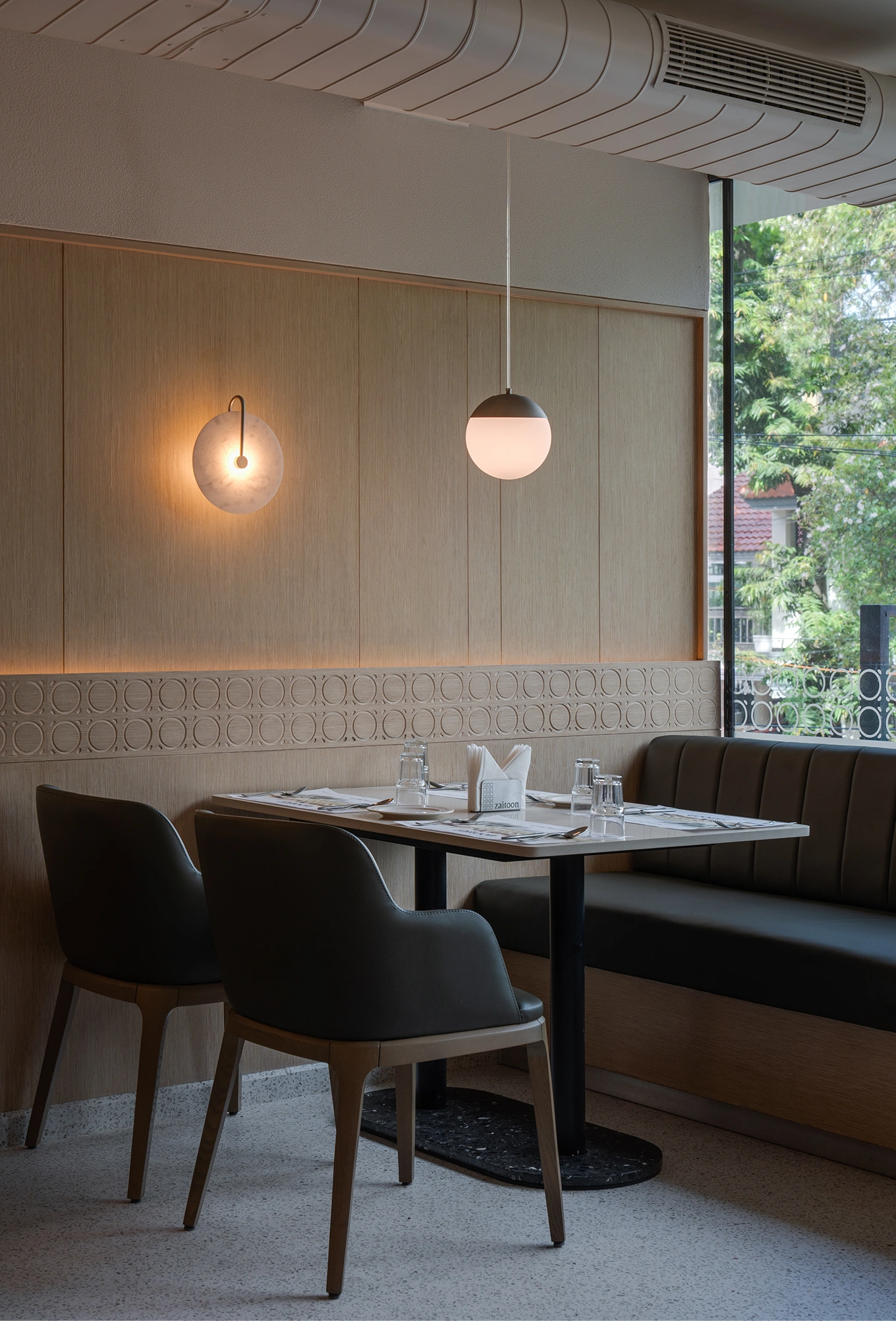 Dining booth with a marble-top table set for two beneath pendant and wall lighting
